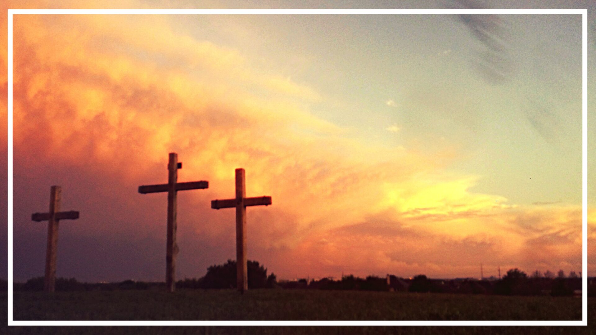 Two crosses in a field with the sky behind them.